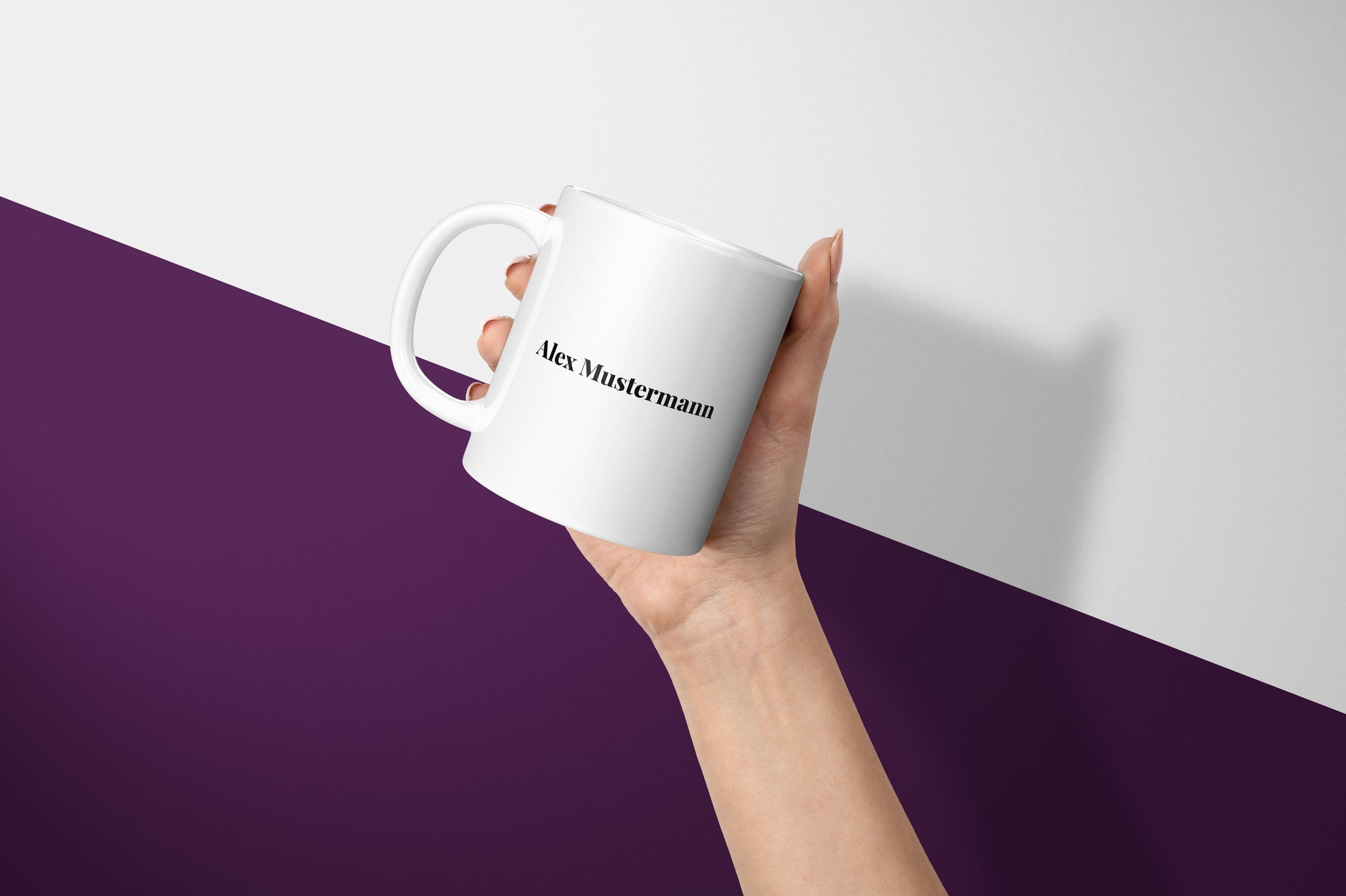 Damenhand mit lackierten Fingernägeln hält eine personalisierte Tasse mit elegantem Schriftzug in Playfair Display.